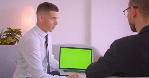 Κοντινό πλάνο του νεαρού επιχειρηματία που δείχνει φορητό υπολογιστή με πράσινη οθόνη αποχρώσεων να εταίρος στο γραφείο σε εσωτερικούς χώρους — Αρχείο Βίντεο