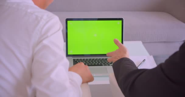 Close-up achteraanzicht portret van twee zakenlui met behulp van laptop met groen scherm met discussie in het kantoor binnenshuis — Stockvideo