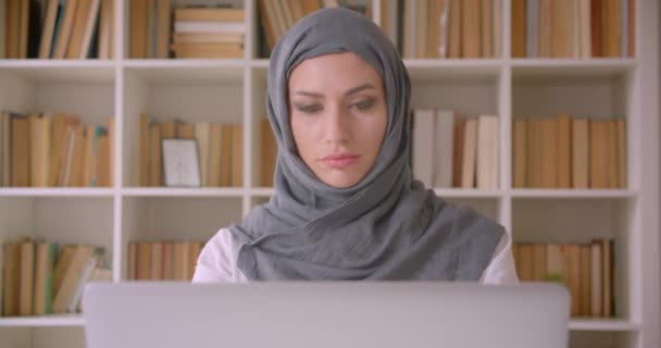 Крупним планом портрет молодої привабливої мусульманської бізнес-леді в хіджабі, використовуючи ноутбук, дивлячись на камеру в бібліотеці в приміщенні — стокове відео