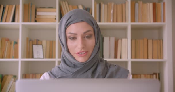 Primer plano retrato de joven atractiva mujer de negocios musulmana en hijab teniendo una videollamada en la biblioteca en el interior — Vídeo de stock
