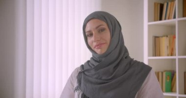 Türbanlı genç çekici Müslüman iş kadınının kapalı ofiste mutlu bir şekilde gülümseyen kameraya bakan closeup portresi