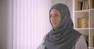 Türbanlı genç çekici Müslüman iş kadınının kapalı ofis tesniyesinde kameraya bakan closeup portresi