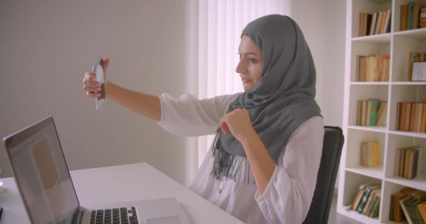 Closeup portré fiatal vonzó muzulmán üzletasszony a hidzsáb vesz selfies telefonon ülve előtt laptop hivatalban beltéri — Stock videók
