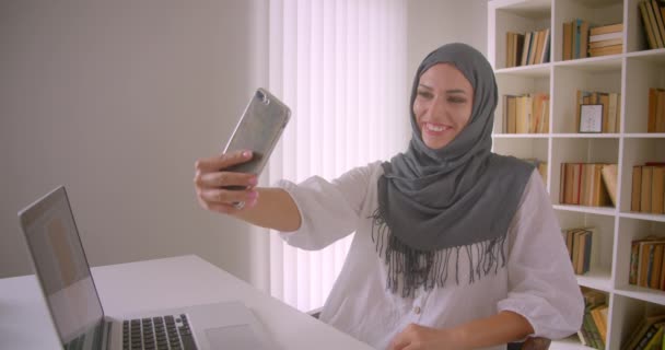 Närbild porträtt av unga glada muslimska affärskvinna i hijab tar selfies på telefon poserar sitter framför laptop i Office inomhus — Stockvideo