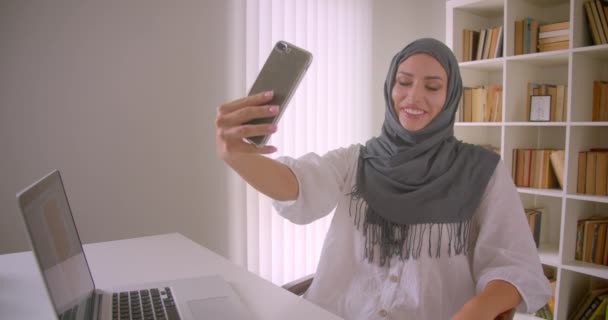 Closeup portrét mladé veselé, velmi muslimské obchodní ženy v hidžábu, která se bude vydávat za telefon, který sedí před laptopem v kanceláři v interiérech