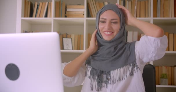Крупним планом портрет молодої привабливої мусульманської бізнес-леді в хіджабі танцює щасливо сидячи перед ноутбуком в офісі в приміщенні — стокове відео