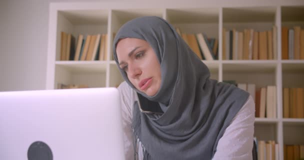 Nahaufnahme Porträt einer jungen attraktiven muslimischen Geschäftsfrau im Hijab mit Laptop, die im Büro telefoniert — Stockvideo