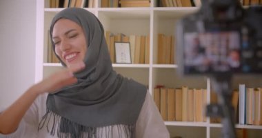 Başörtüsü genç çekici Müslüman blogcu Closeup portre arka planda kitapraflar ile mutlu kapalı gülüyor kamera konuşuyor