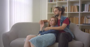 Genç beyaz erkek arkadaşı ve kız arkadaşı kanepede oturan ve evde şefkatle sarılma portre çekimi.