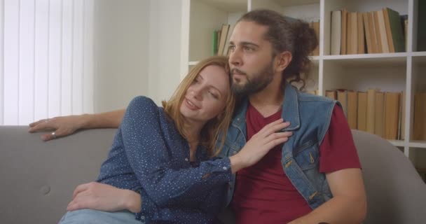 Retrato do jovem namorado e namorada caucasiana sentados no sofá conversando alegremente uns com os outros em casa . — Vídeo de Stock