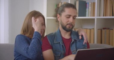 Dizüstü bilgisayar kullanarak kanepede oturan ve evde özenle tartışan genç kendinden emin beyaz çift.