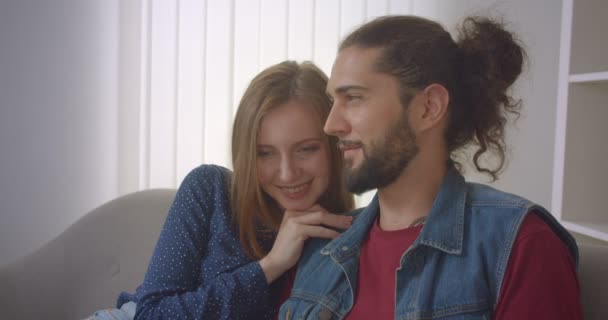 Retrato de la joven pareja hipster sentada en el sofá leyendo el libro y discutiéndolo en casa . — Vídeo de stock