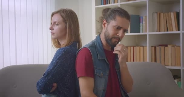 Dos amigos enojados que están en disputa sentados espalda con espalda en el conflicto de sofá entre novia y novio . — Vídeos de Stock