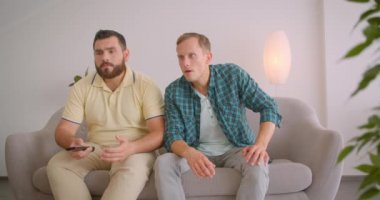 Tv'de futbol seyreden iki yetişkin beyaz erkek arkadaşın evde ki kanepede birlikte otururken kaybettikleri için üzgün olduğu closeup portresi
