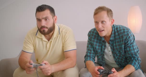 Close-up portret van twee Kaukasische mannen spelen video games samen zittend op de Bank thuis binnenshuis — Stockvideo