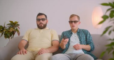 Tv'de korku filmi izleyen iki beyaz komik adamın kapalı mekanda birlikte kanepede otururken ki yakın çekim portresi