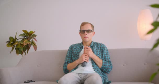 Крупним планом портрет білоруського смішного чоловіка, який дивиться фільм жахів по телевізору, сидячи на дивані — стокове відео