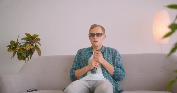 Closeup portrait of caucasian funny man watching horror movie on TV sitting on couch and being scared by his friend indoors — Stock Video