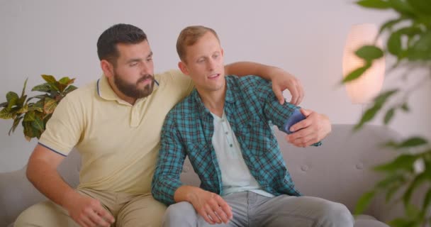 Retrato de close-up de dois homens caucasianos tomando selfies no telefone sentado no sofá juntos em casa aconchegante dentro de casa — Vídeo de Stock