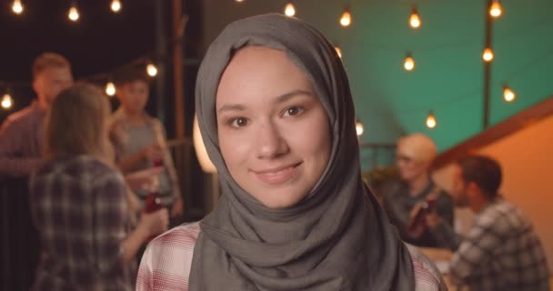 Primer plano retrato de joven bastante musulmana hembra en hijab mirando la cámara en la fiesta diversa en la noche acogedora — Vídeos de Stock
