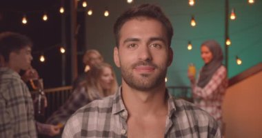 Genç yakışıklı beyaz adamın samimi bir akşamda farklı partide mutlu bir şekilde gülümseyen kameraya bakan yakın çekim portresi