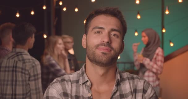 Closeup portrait of young handsome caucasian man looking at camera smiling cheerfully at diverse party in cozy evening — Stock Video