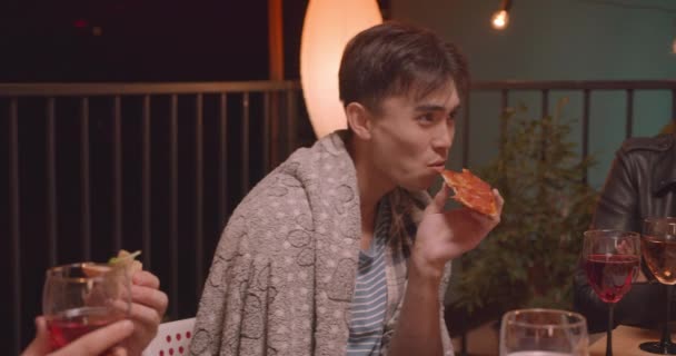 Крупним планом портрет різноманітної багаторасової групи друзів, які їдять піцу на прохолодній вечірці в затишний вечір з казковим вогнем на фоні — стокове відео
