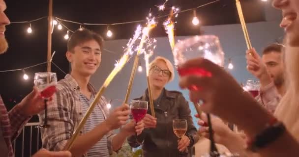 Zbliżenie portret różnorodnych wielogasecznych Wesoła Grupa przyjaciół obchodzi szczęśliwie Picie wina paluszki fajerwerki na imprezie zabawa w przytulnym wieczorem — Wideo stockowe