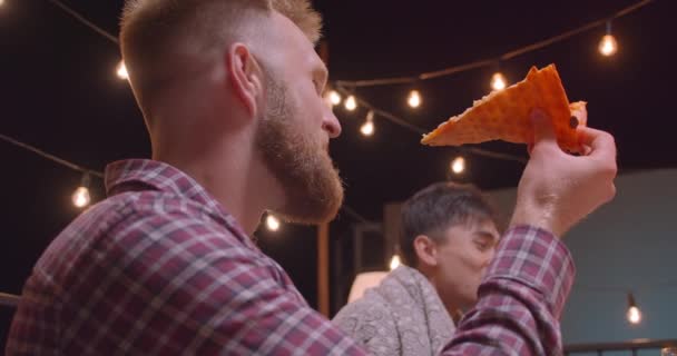 Close-up portret van de man eten pizza in diverse multiraciale groep vrienden op cool feest in gezellige avond met Fairy lichten op achtergrond — Stockvideo