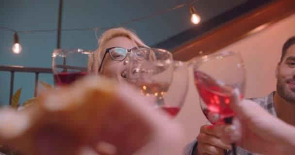 Крупный план портрета многонациональной группы друзей, пьющих красное вино и поедающих пиццу в уютный вечер с волшебными огнями на заднем плане — стоковое видео