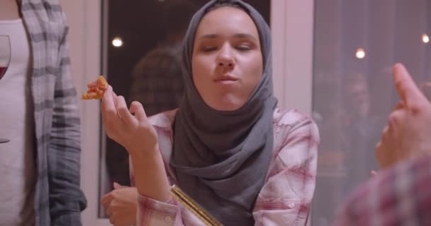 Close-up portret van moslim vrouwelijke eating pizza divers multiraciale groep vrienden met Fairy lichten op achtergrond — Stockvideo