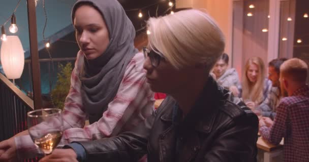 Close-up portret van twee vrouwen praten privé met gevarieerde multiraciale groep vrienden op de achtergrond op feest — Stockvideo