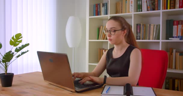 Primer plano retrato de la joven mujer de negocios pelirroja bonita en gafas usando el ordenador portátil y conseguir sorprendido en la oficina en el interior — Vídeo de stock