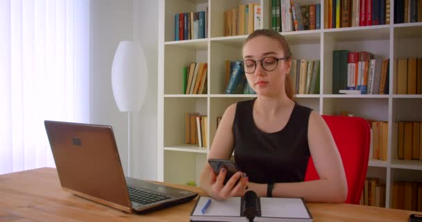 Ofiste dizüstü bilgisayar önünde oturan kameraya yeşil ekran gösteren telefon kullanarak gözlük genç güzel kızıl başlı iş kadının Closeup portre — Stok video