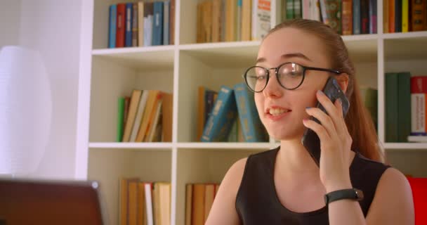 Primer plano retrato de la joven empresaria pelirroja de éxito en gafas usando el ordenador portátil que tiene una llamada telefónica hablando alegremente en la oficina en el interior — Vídeos de Stock