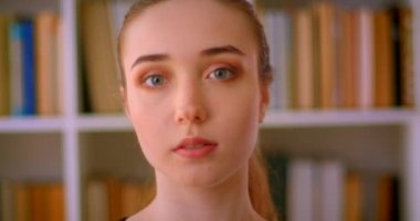 Genç güzel kızıl saçlı kız öğrencinin kapalı kütüphanede kameraya bakan closeup portresi