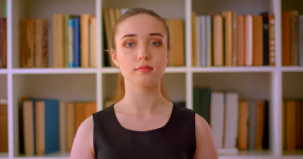 Closeup portrét mladé úspěšné ženské studentky, která se vesele dívá na kameru do knihovny uvnitř s policemi na pozadí — Stock video