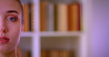 Kapalı kütüphanede kameraya bakan genç güzel kız öğrencinin Closeup yarım yüz portresi