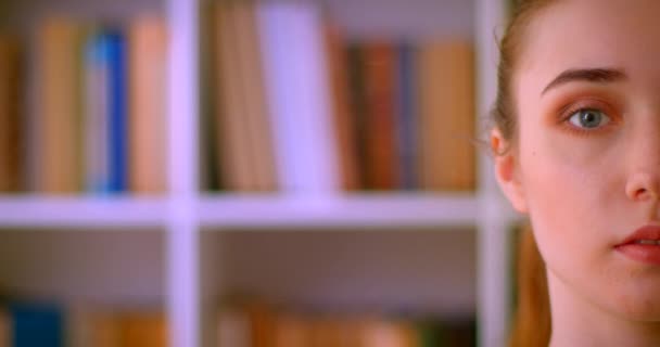 Närbild Half Face porträtt av ung vacker rödhårig kvinnlig student tittar på kamera i biblioteket inomhus — Stockvideo