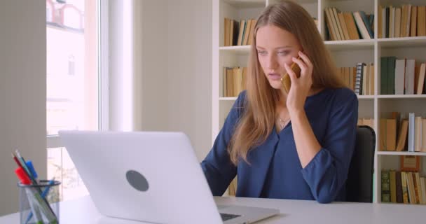 Primer plano retrato de joven exitoso atractiva mujer de negocios caucásica utilizando el ordenador portátil que tiene llamadas telefónicas tomando notas en la oficina en el interior — Vídeo de stock