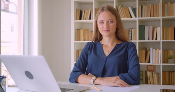 Primer plano retrato de joven atractiva mujer de negocios caucásica utilizando el ordenador portátil mirando a la cámara sonriendo felizmente sentado en el escritorio en la oficina en el interior — Vídeos de Stock