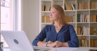 Genç çekici beyaz iş kadını kapalı ofis dizüstü ile masada neşeyle otururken gülümseyen kameraya bakarak closeup portre