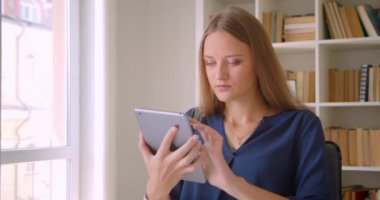 Tablet kullanan ve ofiste masada oturan kameraya yeşil renk ekranı gösteren genç çekici kafkas iş kadınının yakın çekim portresi