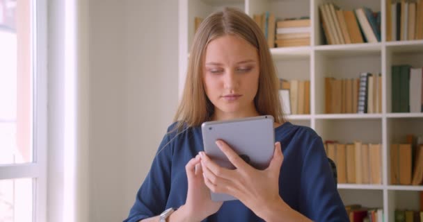 Retrato de close-up de jovem atraente mulher de negócios caucasiana usando tablet e mostrando tela verde para câmera sentada na mesa no escritório dentro de casa — Vídeo de Stock