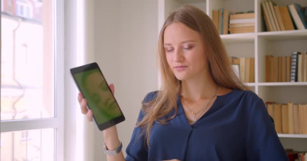 태블릿을 사용하여 사무실에서 책상에 앉아 카메라에 녹색 크로마 키 화면을 보여주는 젊은 매력적인 백인 사업가의 클로즈업 초상화 — 비디오