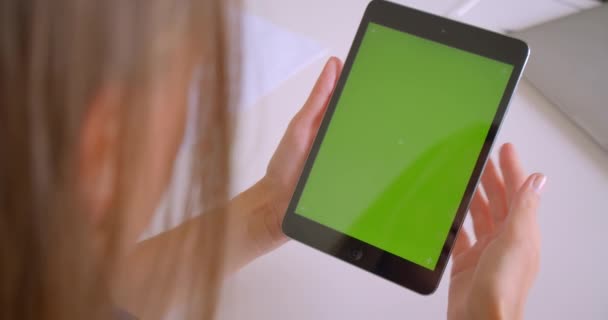 Close-up achteraanzicht portret van jonge aantrekkelijke blanke vrouw het gebruik van een tablet met een groen Chroma-toetsen scherm in Office binnenshuis — Stockvideo