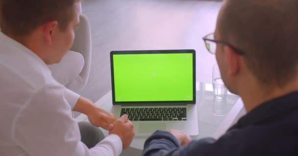사무실 실내에서 안락 의자에 앉아 회의를 갖는 노트북을 사용하여 두 사업가의 클로즈업 백뷰 초상화 — 비디오
