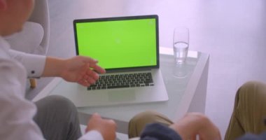Yeşil renk ekranlı dizüstü bilgisayar kullanan iki işadamının yakın çekim arka görüş portresi kapalı ofis koltuklarında oturan bir toplantı