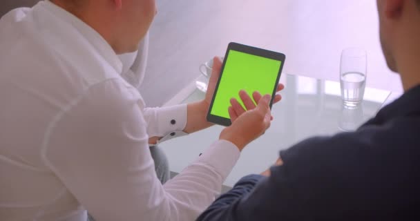 Close-up achteraanzicht portret van twee zakenlui met behulp van tablet met groen Chroma toetsen scherm een vergadering zittend in Fauteuils in kantoor — Stockvideo