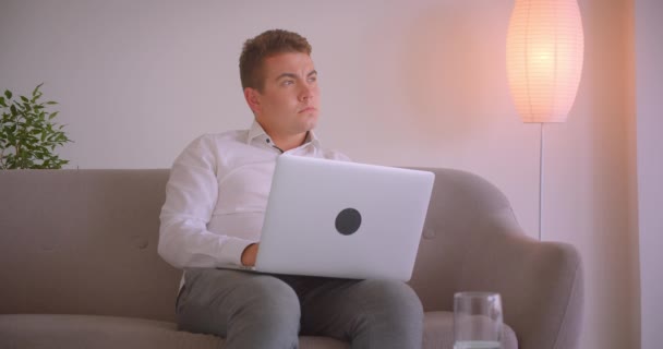 실내 사무실에서 소파에 앉아 노트북을 사용하여 성인 백인 사업가의 클로즈업 초상화 — 비디오